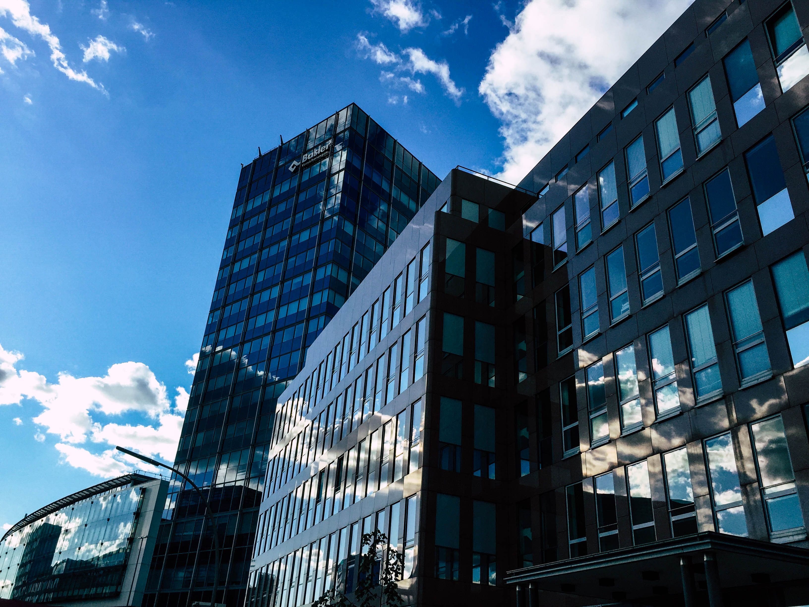 Low-angle view of modern glass skyscrapers reflecting a bright blue sky and white clouds.