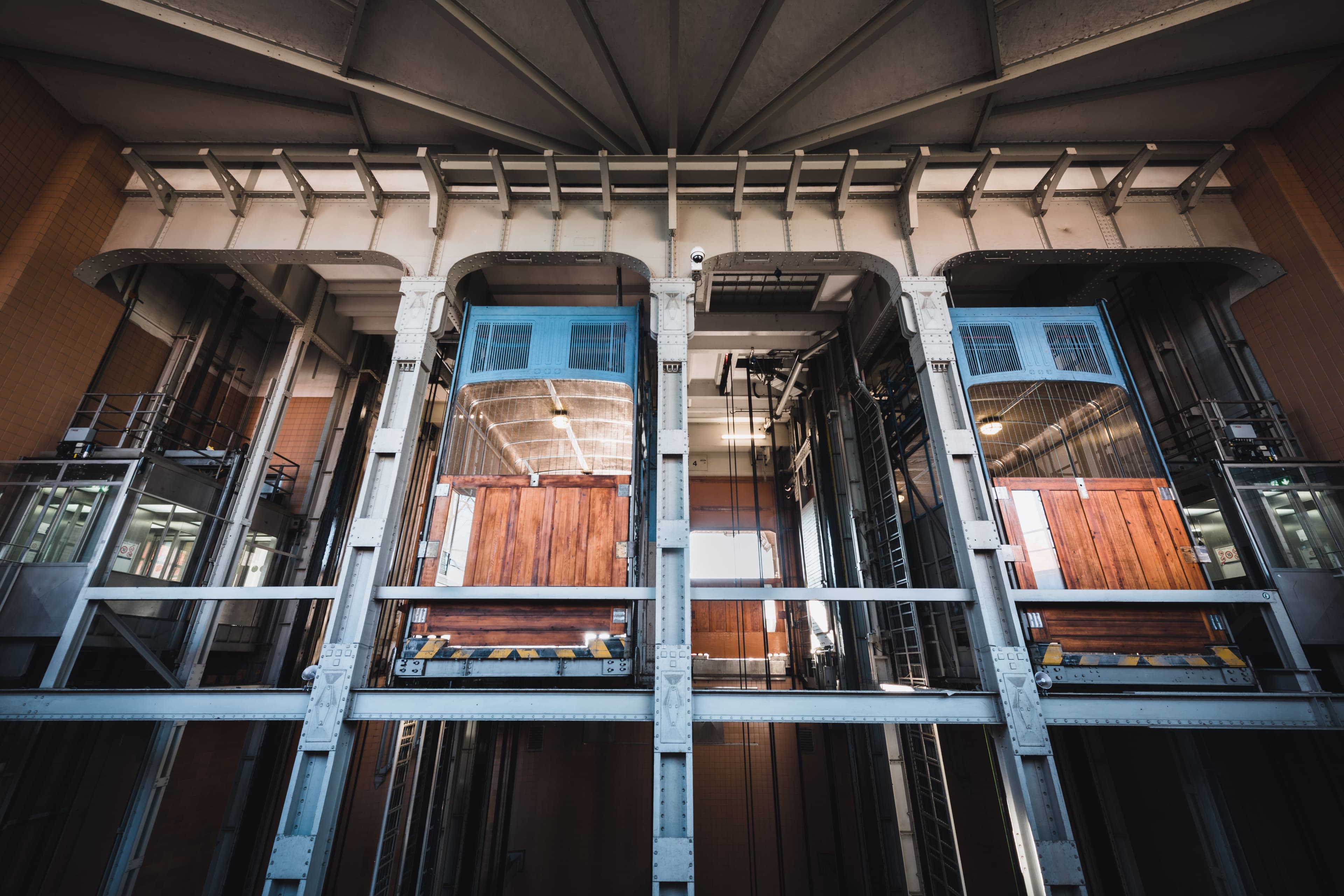 Vintage wooden elevators with blue metal frames housed within a massive industrial steel structure.