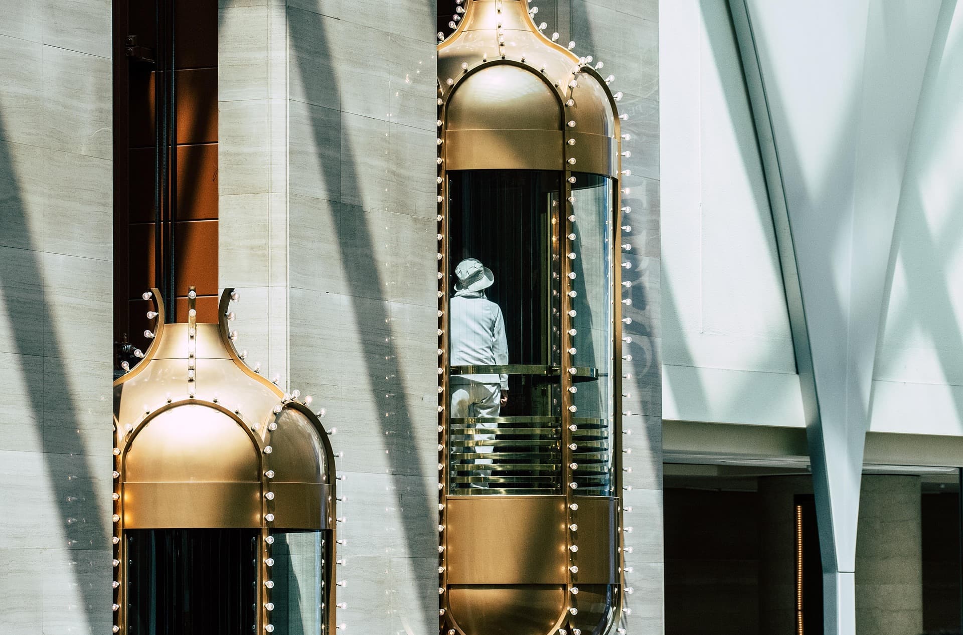 Gold capsule elevators lined with lights, one holding a person in white, in a modern building.